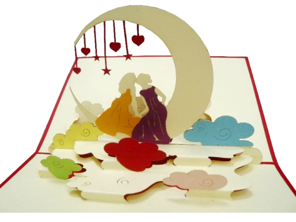 Klappkarte: Hochzeit - Mrs & Mrs Eine Klappkarte aus Papier, die aufgeklappt ist und ein Paar aus zwei Freuane mit einem gelben und einem roten Kleid unter einem Bogen mit herabhängenden Herzen zwischen bunten Wolken zu sehen ist.